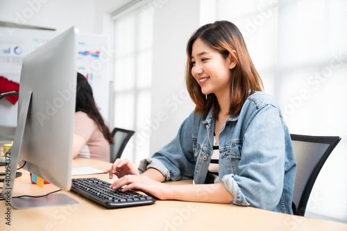 Young asian beautiful woman working on computer at workplace with a business team group