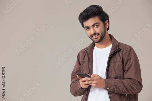 A YOUNG MAN LOOKING AT CAMERA AND SMILING WHILE USING MOBILE PHONE	 photo