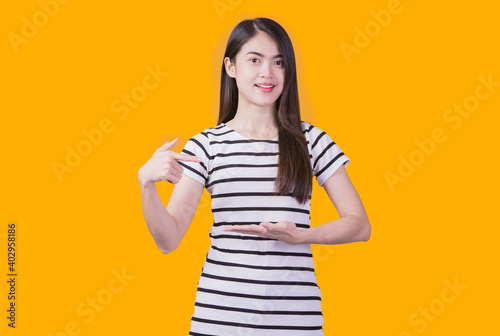 Smiling asian woman pointing up and looking at the camera over yellow background