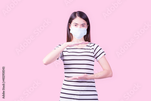 Studio image of a woman wearing a mask looking at the camera separately on a pink background. Flu epidemic, dust allergy, COVID-19 prevention, health and hygiene concept.