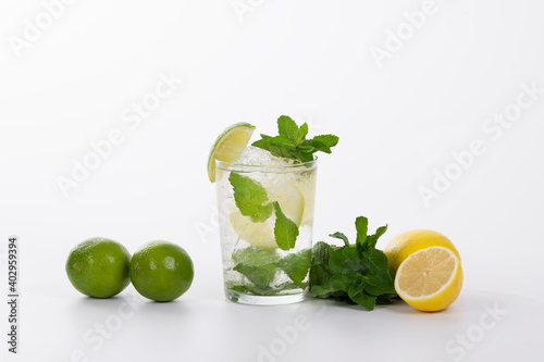 view of a refreshing mojito cocktail surrounded by limes, lemons and fresh mint leaves