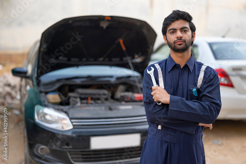 A YOUNG MECHANIC HOLDING TOOLS STANDING IN FRONT OF AN OPEN CAR  © IndiaPix