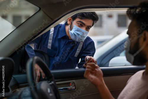 A MECHANIC WEARING FACE MASK TALKING TO A CUSTOMER SITTING IN CAR 