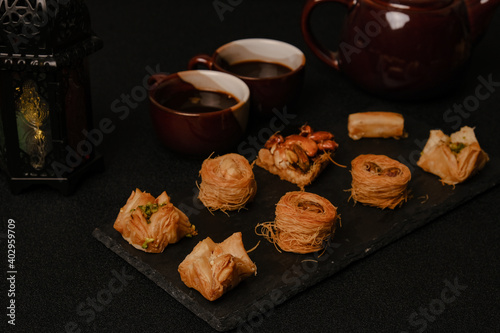A low key and selective focus picture of Arabic baklava on slate plate with cup, teapot and lantern insight.