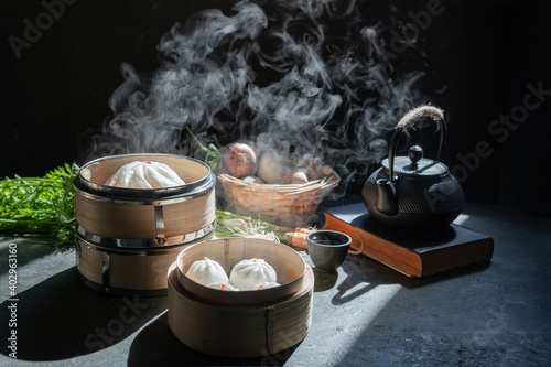 Bilde på lerret Chinese steamed buns on a plate and bamboo baskets on  black wooden table with tea time ( dim sum, yam cha , pao ) bao sa la pao