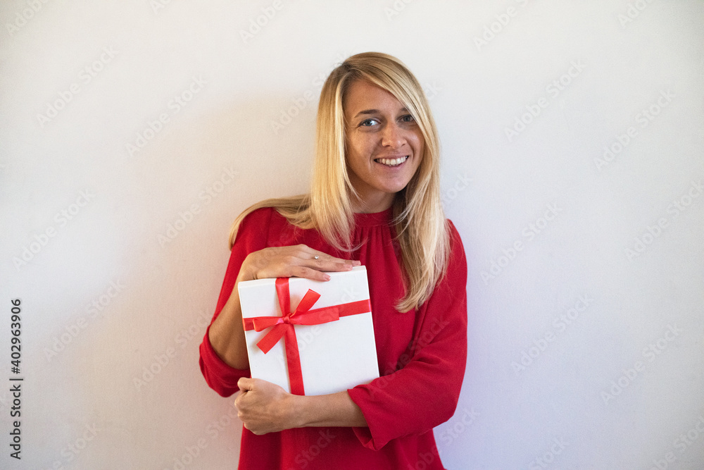 Young woman holds gift box white color with red tape. Person cute smiles and delight. Girl wearing red blouse on white background. In Lovely Valentine day in 14th February get a gift. celebration Young woman holds gift box white color with red tape. Person cute smiles and delight. Girl wearing red blouse on white background. In Lovely Valentine day in 14th February get a gift. celebration