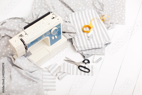process of sewing of bed linen on sewing machine. Sewing kit. Grey fabric, scissors, threads, measuring tape and sewing machine on white wooden background