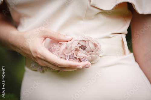 Woman touch beautiful handmade cincture, beige color. Close up. Belt, embroidered with beads and fabric flowers. Bride's hand touching details of her wedding dress