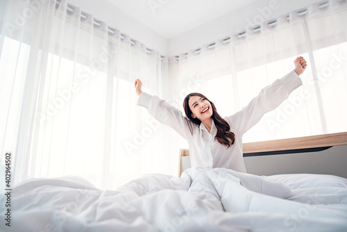 Happy asian woman stretching hands in bed after wake up in the morning, Concept of a new day and joyful weekend.