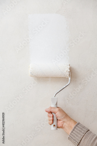 Painting roller in worker's hand. Repair in a room. Painting of walls. Woman is painting the wall