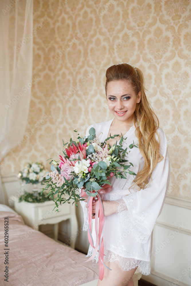 Pretty young Bride. Blonde-haired woman with wedding hair-style with a long tail. Boudoir morning of the bride. Looking on her bouquet Pretty young Bride. Blonde-haired woman with wedding hair-style with a long tail. Boudoir morning of the bride. Looking on her bouquet