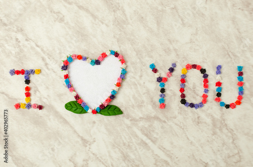 I love you, written with flowers on a marble table. Blank heart-shaped card framed with flowers.