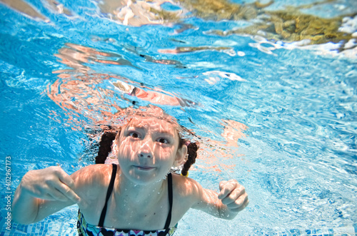 Little child swims underwater in swimming pool  happy active baby girl dives and has fun under water  kid fitness and sport  