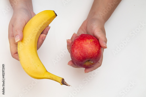 Foto Top view of female hands holding and comparing between red apple and banana isol