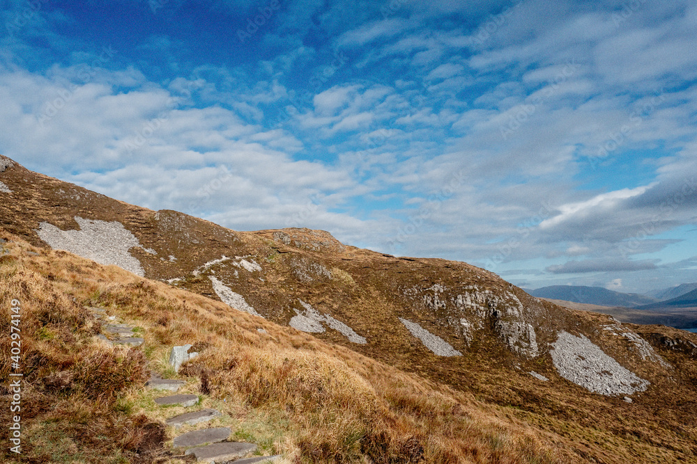 View from Diamond hill in Connemara National park, county Galway, Ireland, Small walking path. Bright sunny day, blue cloudy sky. Mountains in the background View from Diamond hill in Connemara National park, county Galway, Ireland, Small walking path. Bright sunny day, blue cloudy sky. Mountains in the background
