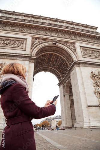 Woman using smartphone next to Arc de Triomphe, triumphal arch, one of Paris symbols. © astrosystem
