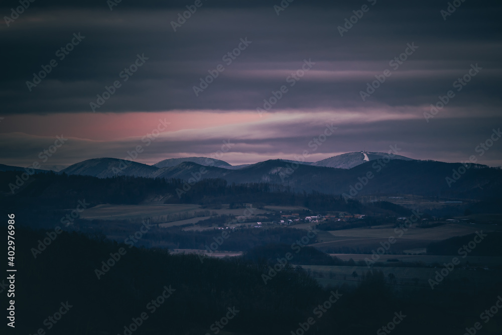 Sunset dark sky with clouds over the mountainous landscape of Pustevny lying under the fog in a dark color.