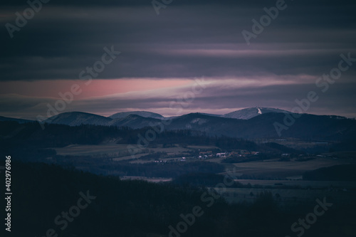 Sunset dark sky with clouds over the mountainous landscape of Pustevny lying under the fog in a dark color. © Lukas