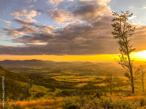 A view of a landscape full of mountains during a golden sunset with the sun on the horizon and a view of the sun from the top of Mount Ondrejnik. photo