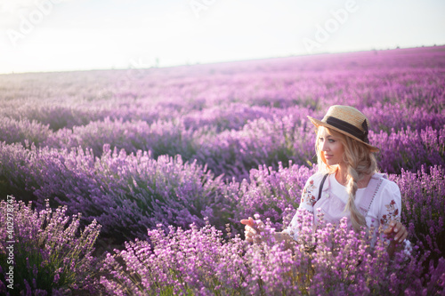 Portrait of beautiful blond woman with long curl hair relax in the purple field with lavender flowers. Woman walking in the sunrise and breathes the scent of Provencal herbs