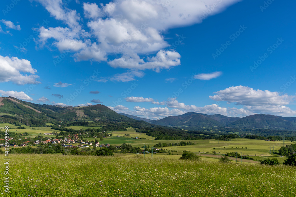 Naklejka premium Under the sun and shadows Ondřejník and a view of other Beskydy hills and mountains with white clouds and blue sky in the background.