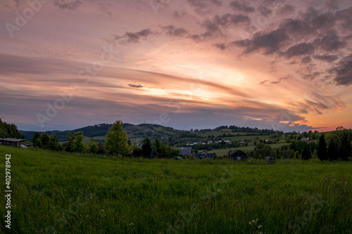 Landscape full of hills and mountains with clouds and blue sky with sun during colorful sunset Beskydy region.