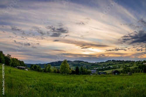 Landscape full of hills and mountains with clouds and blue sky with sun during colorful sunset Beskydy region.