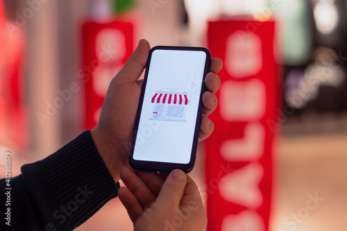 A man holds a smartphone in his hands with icon on the display. Super Sale against the background of a shop window of a clothing store.