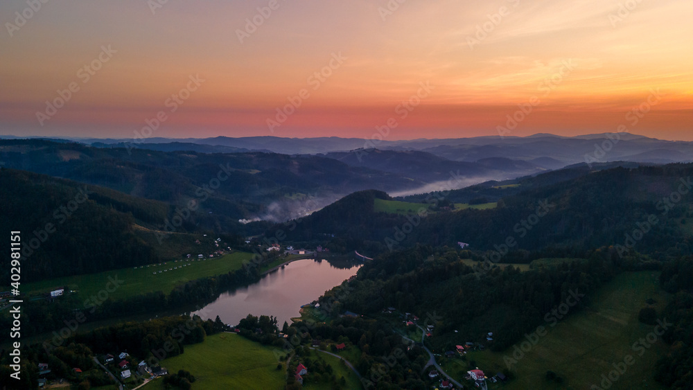 Aerial view of a hill on the Bystricka dam and the surrounding hills during sunset between the valley appears fog.
