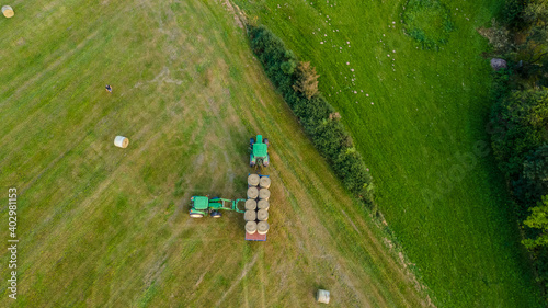 Aerial view of agricultural machinery while cleaning hay bales on a green hill.