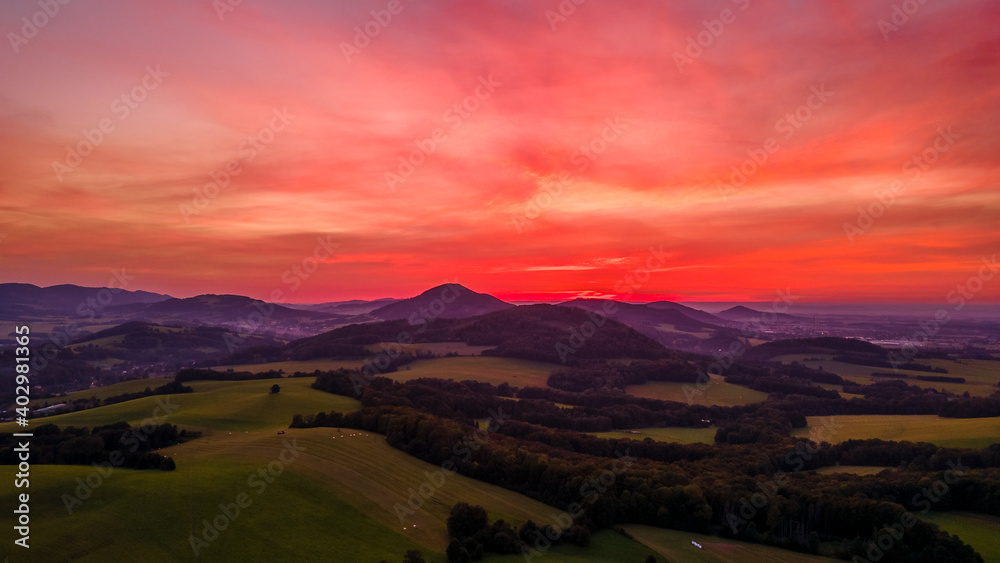 Aerial view of colorful clouds and mountainous hilly landscape at sunset over the horizon of Beskydy region.