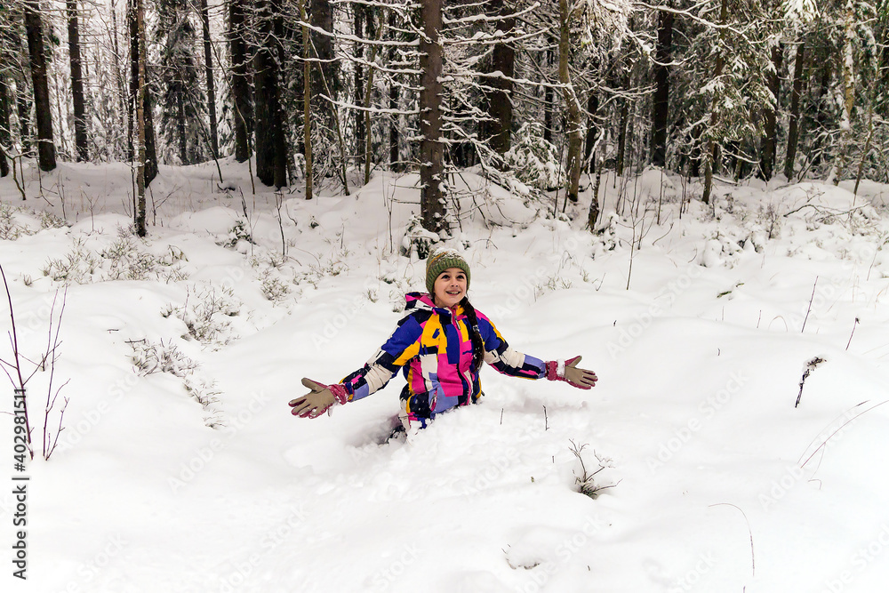 A happy cheerful girl climbed into a snowdrift on a walk outside the city in the forest.