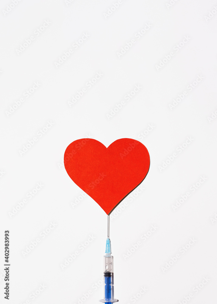 Safe vaccination concept with place for text on top. Syringe with vaccine and a big red heart on a white background, top view. Vertical perspective Safe vaccination concept with place for text on top. Syringe with vaccine and a big red heart on a white background, top view. Vertical perspective