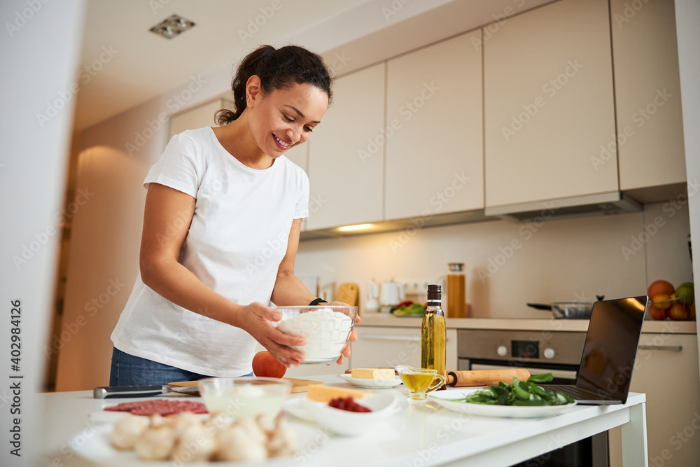 Mirthful lady smiling and making dough for the meal