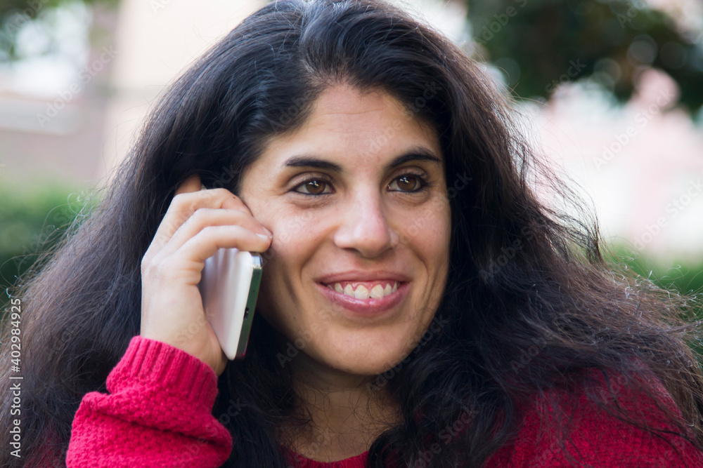 Latin American young adult woman laughing with long dark hair and talking on the mobile phone Latin American young adult woman laughing with long dark hair and talking on the mobile phone