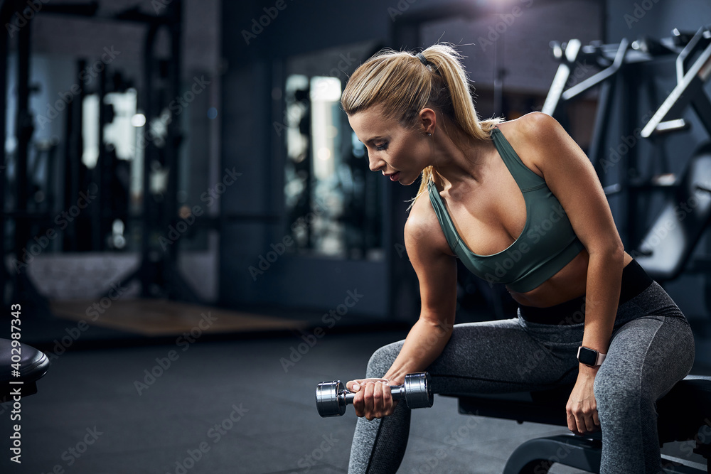 Sportive female leaning ahead and lifting a hand weight Sportive female leaning ahead and lifting a hand weight