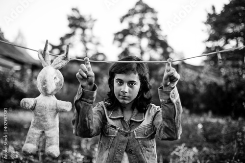 Teen girl dries a toy hare on a clothesline. Black and white photo.