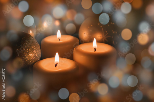 White Christmas candles are burning, green fir branches are lying next to them, Christmas toys, festive highlights of garlands and the flame of three candles give a sense of celebration. © Chitorok