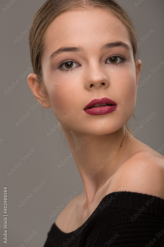 portrait of a beautiful teen girl with exquisite makeup with red lipstick on a gray background