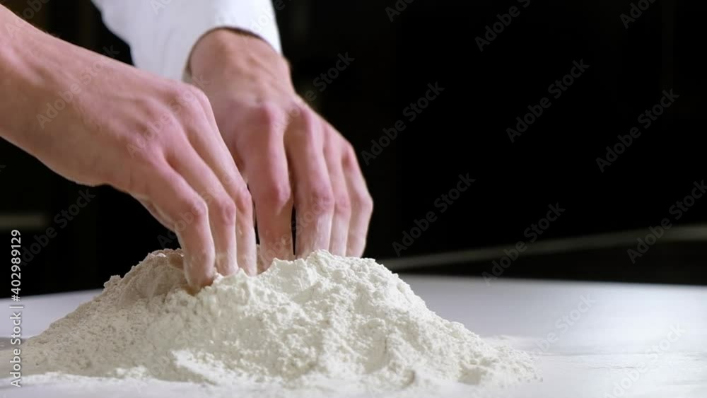 Professional baker works in kitchen of bakery shop. cook makes slide of white wheat flour with his hands to start making dough. Baking bread or pizza or pie. Professional baker works in kitchen of bakery shop. cook makes slide of white wheat flour with his hands to start making dough. Baking bread or pizza or pie.