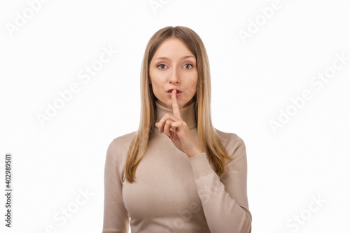 Portrait of young blond woman keeping finger at her mouth, saying Shh, Hush, Tsss. Silence and secret concept