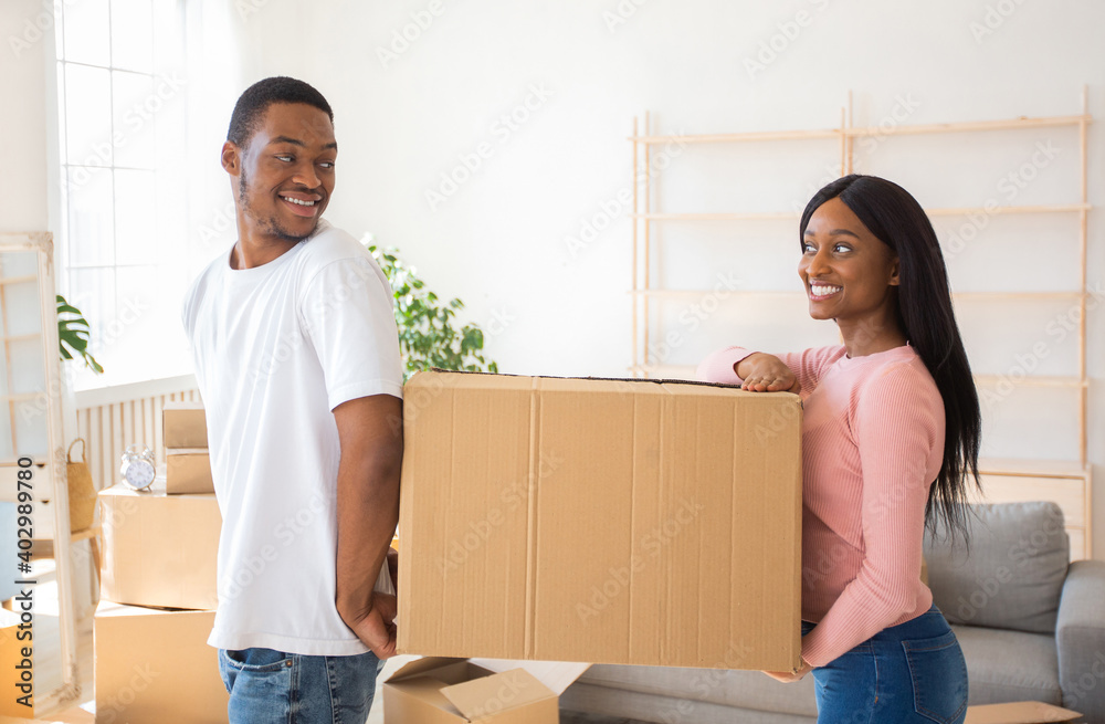 Home relocation concept. Friendly black couple with carton box relocating to new home, copy space