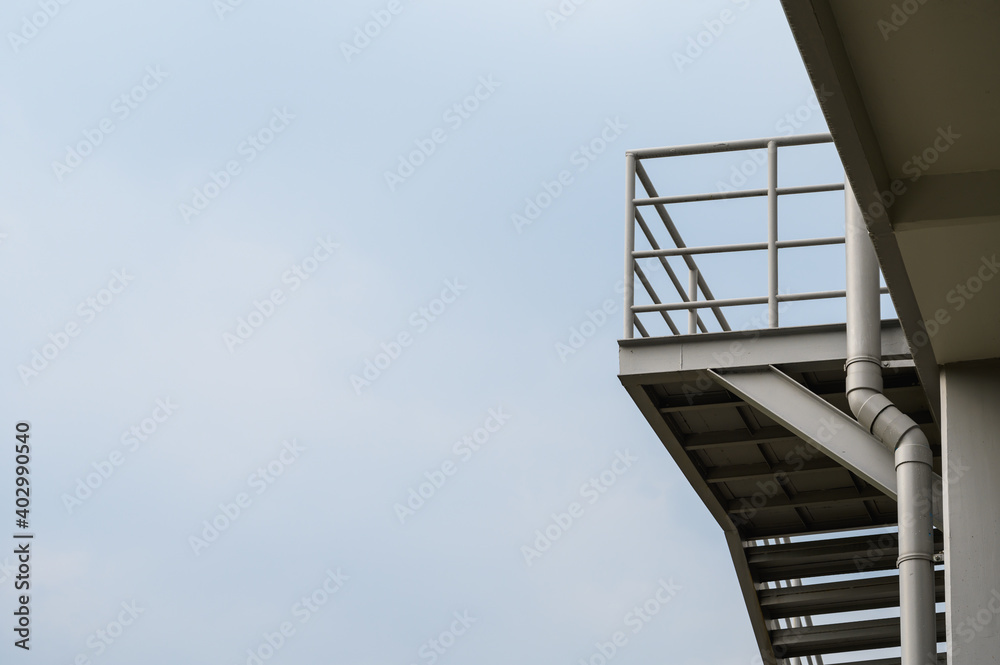 Fototapeta premium Exterior metal staircase of the building with cloud sky in background. Outdoors staircase of the building.