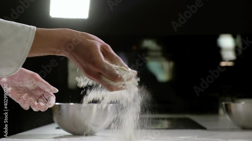 Uniformed chef works baker in restauran kitchen. man sprinkles white wheat flour with hand on table for making dough for traditional national pizza. Preparation of ingredients for making pizza dough.