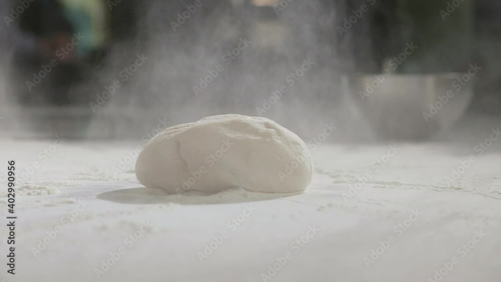 Young chef works as baker in restaurant's kitchen. man sprinkles raw dough with wheat flour on table for making traditional national pizza. Preparation of ingredients for making pizza dough.