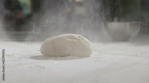 Young chef works as baker in restaurant's kitchen. man sprinkles raw dough with wheat flour on table for making traditional national pizza. Preparation of ingredients for making pizza dough.