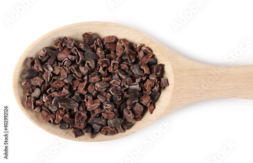 Chopped, grated cocoa pieces in wooden spoon isolated on white background, top view