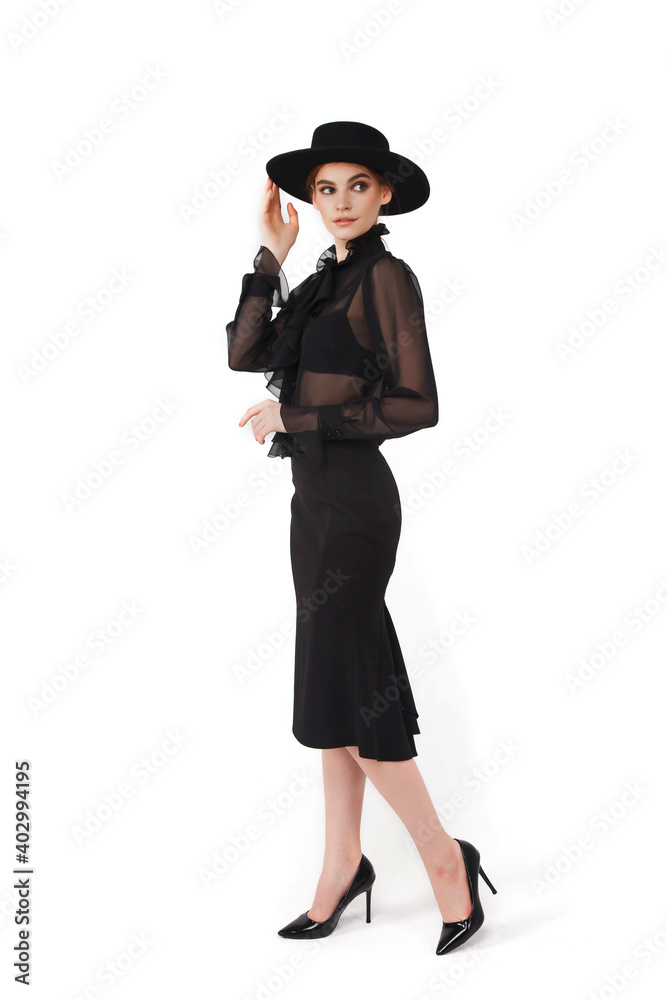 Stylish cute young businesswoman in black elegant blouse and hat on white isolated background. Woman in fashionable clothes posing at camera. Concept of style, fashion, beauty and achievement of goals