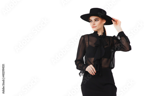 Stylish cute young businesswoman in black elegant blouse and hat on white isolated background. Woman in fashionable clothes posing at camera. Concept of style, fashion, beauty and achievement of goals