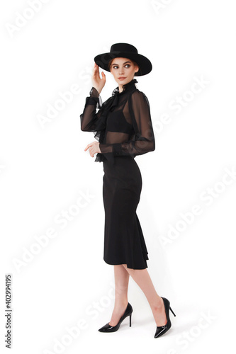 Stylish cute young businesswoman in black elegant blouse and hat on white isolated background. Woman in fashionable clothes posing at camera. Concept of style, fashion, beauty and achievement of goals